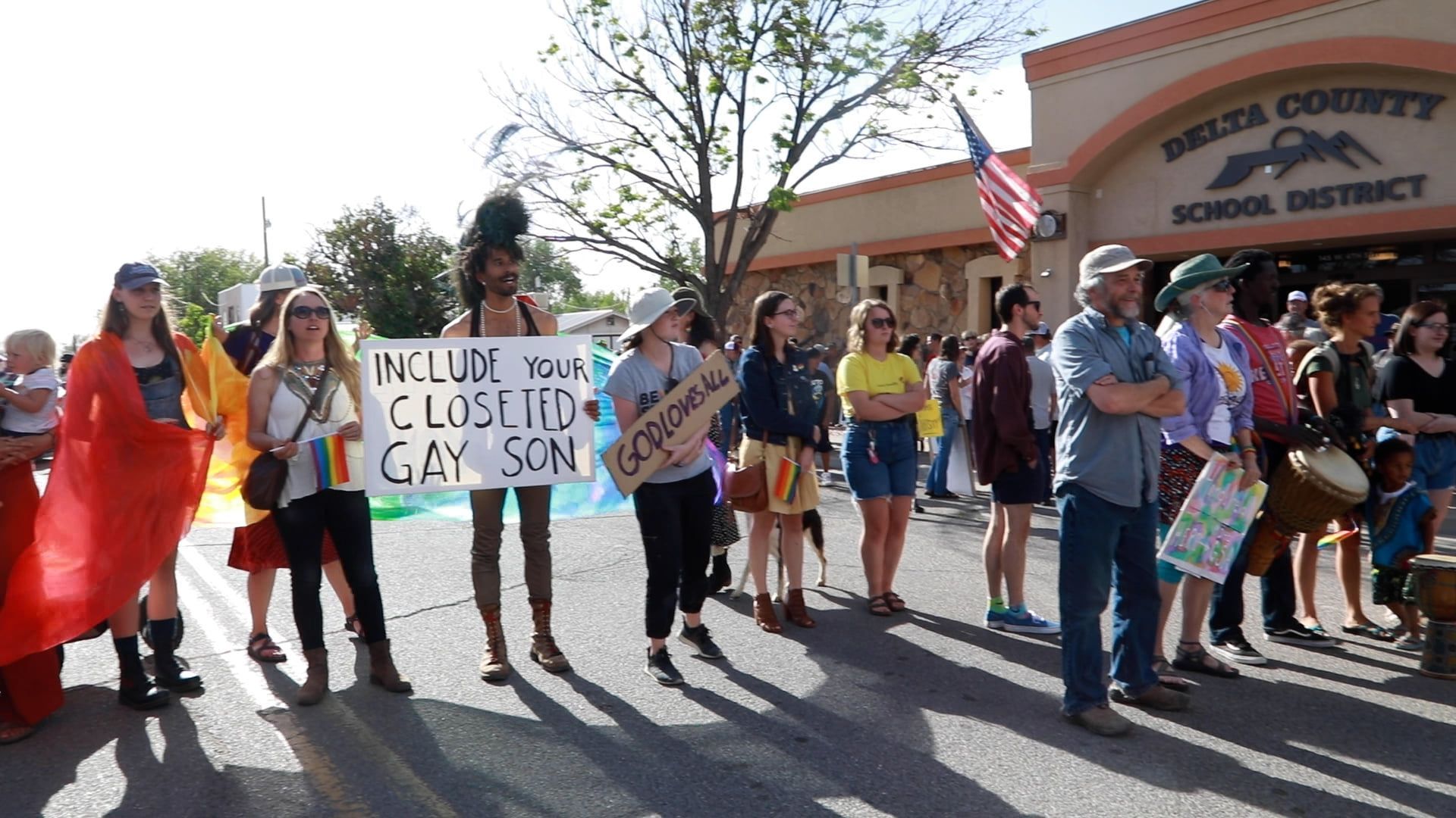 People holding signs and rainbow flags outside a school district building during a protest