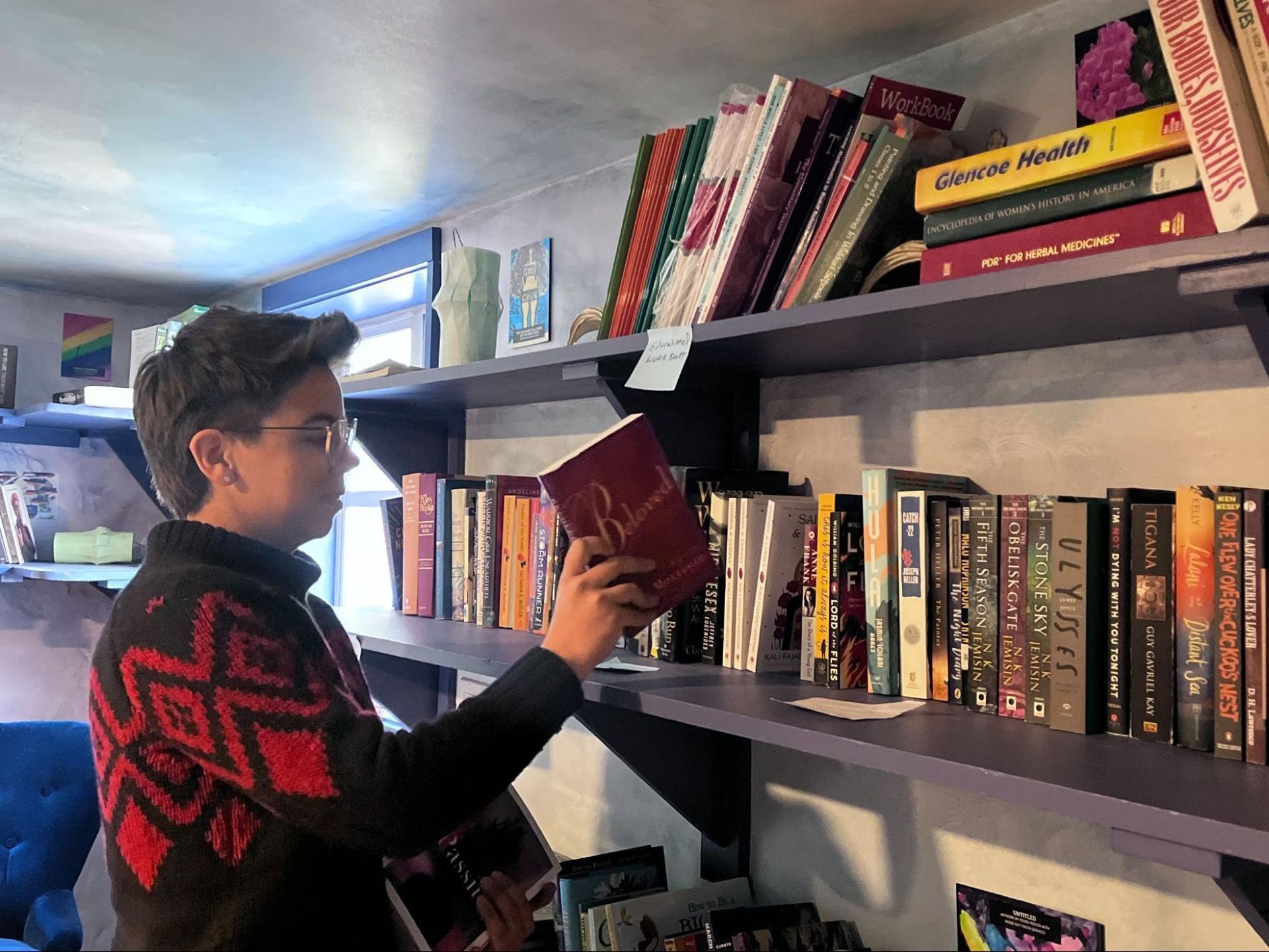 Person browsing books on a shelf in a bookstore, wearing a black sweater with red patterns.