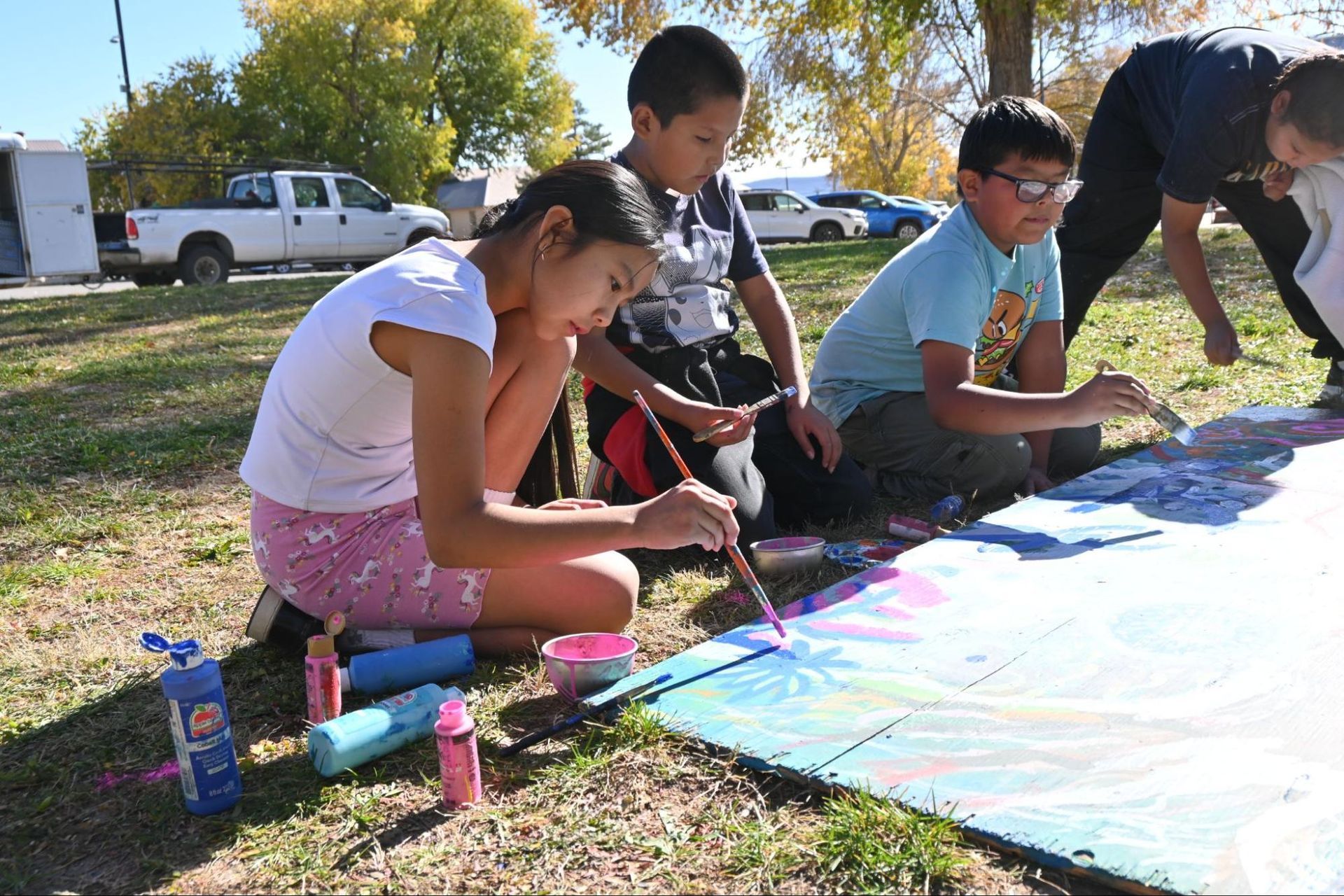 Children painting a large mural outdoors on canvas spread across the grass
