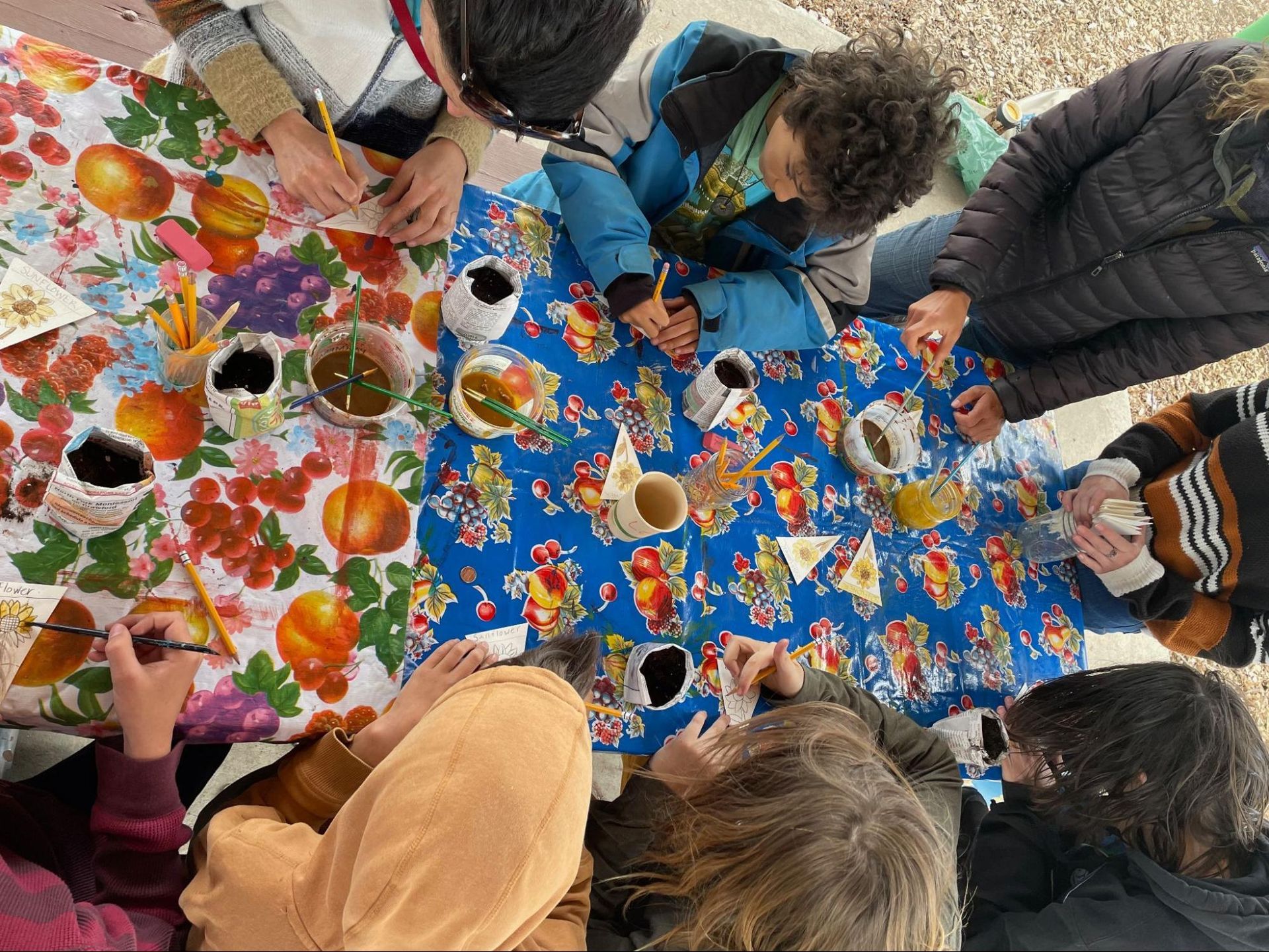 Children gathered around colorful painted cloths outdoors, creating a circle art project.
