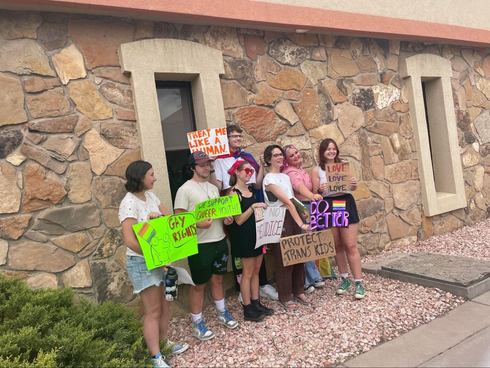 Group of people holding colorful protest signs standing outside a stone building