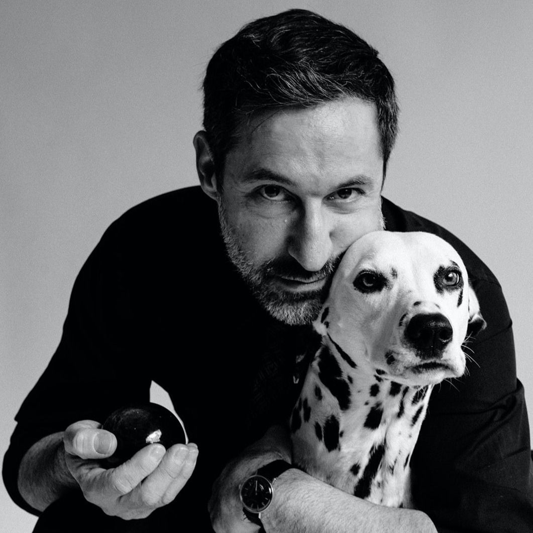 Man holding a black-and-white Dalmatian puppy against a plain gray background