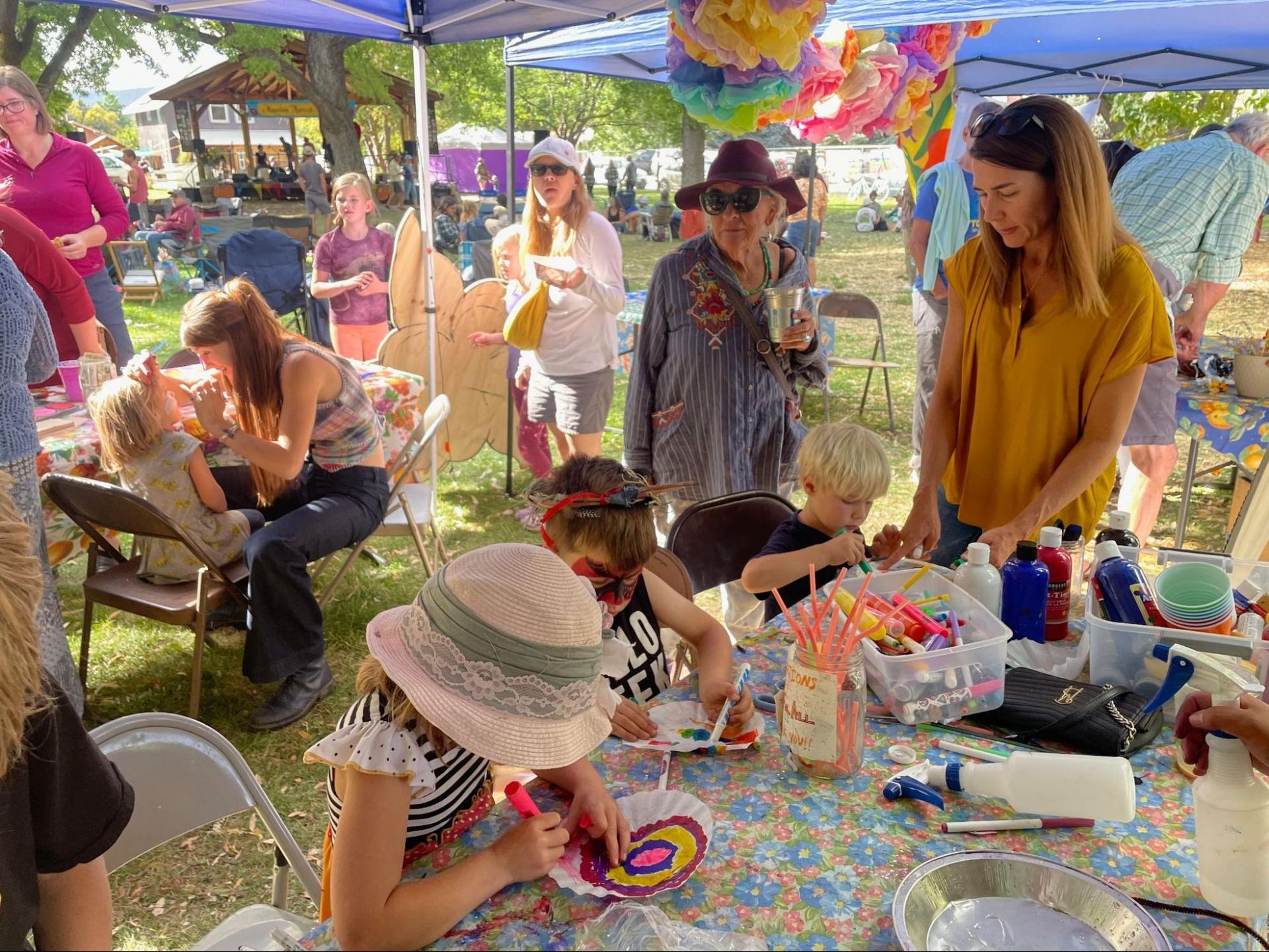 People browsing colorful toys and crafts at an outdoor market stall under a blue canopy