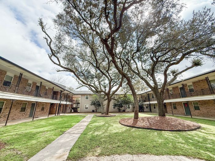 pensacola apartment complex with metal railing on 2nd floor and large pine trees in courtyard