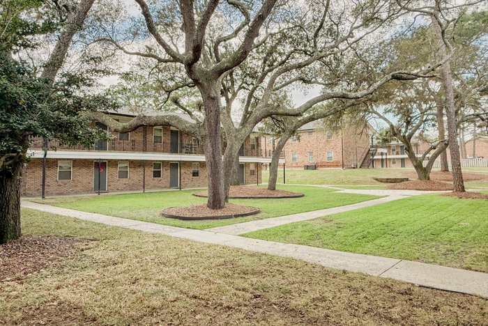 pensacola apartment complex with metal railing on 2nd floor and large pine trees in courtyard