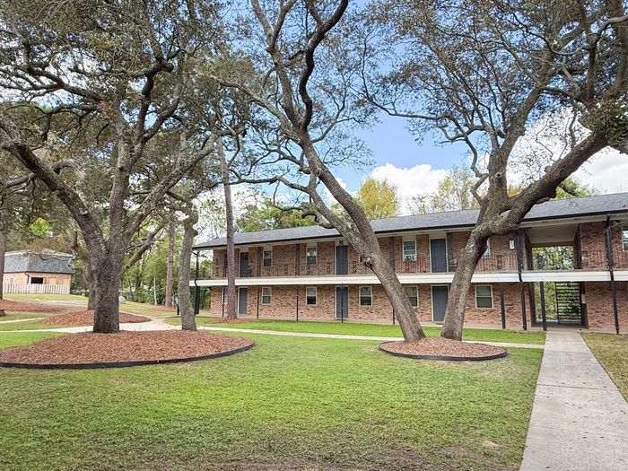 pensacola apartment complex with metal railing on 2nd floor and large pine trees in courtyard