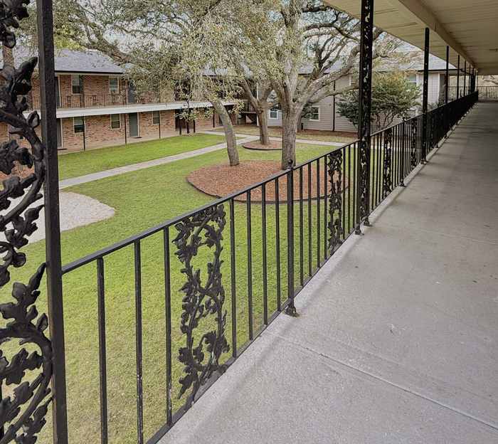 pensacola apartment complex with metal railing on 2nd floor and large pine trees in courtyard