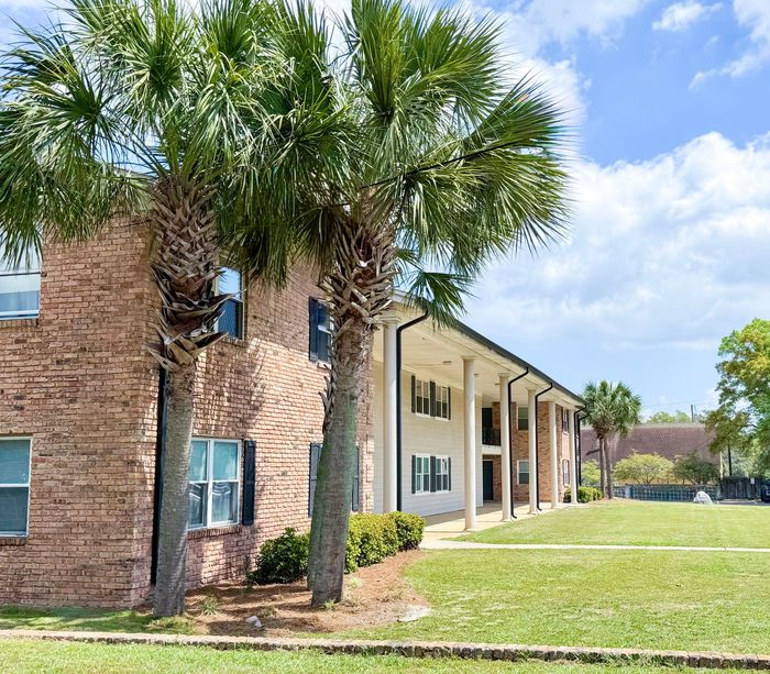 pensacola apartment complex with large pillars and two palm trees at the corner