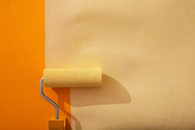 A paint roller is being used to paint an orange wall.