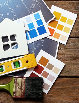 A wooden table topped with a model house , paint samples , a level , and a brush.
