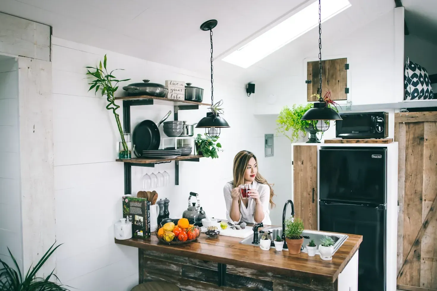A woman is sitting at a counter in a kitchen drinking coffee.