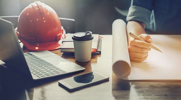 A person is sitting at a desk with a laptop and a hard hat.