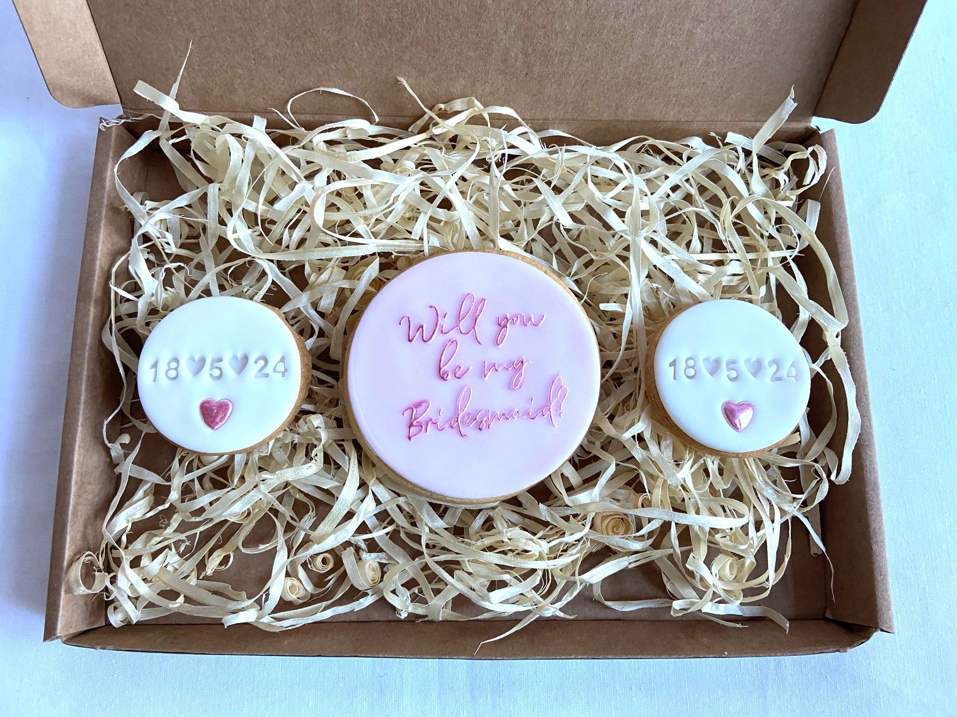 A box filled with straw and cookies that say will you be my bridesmaid