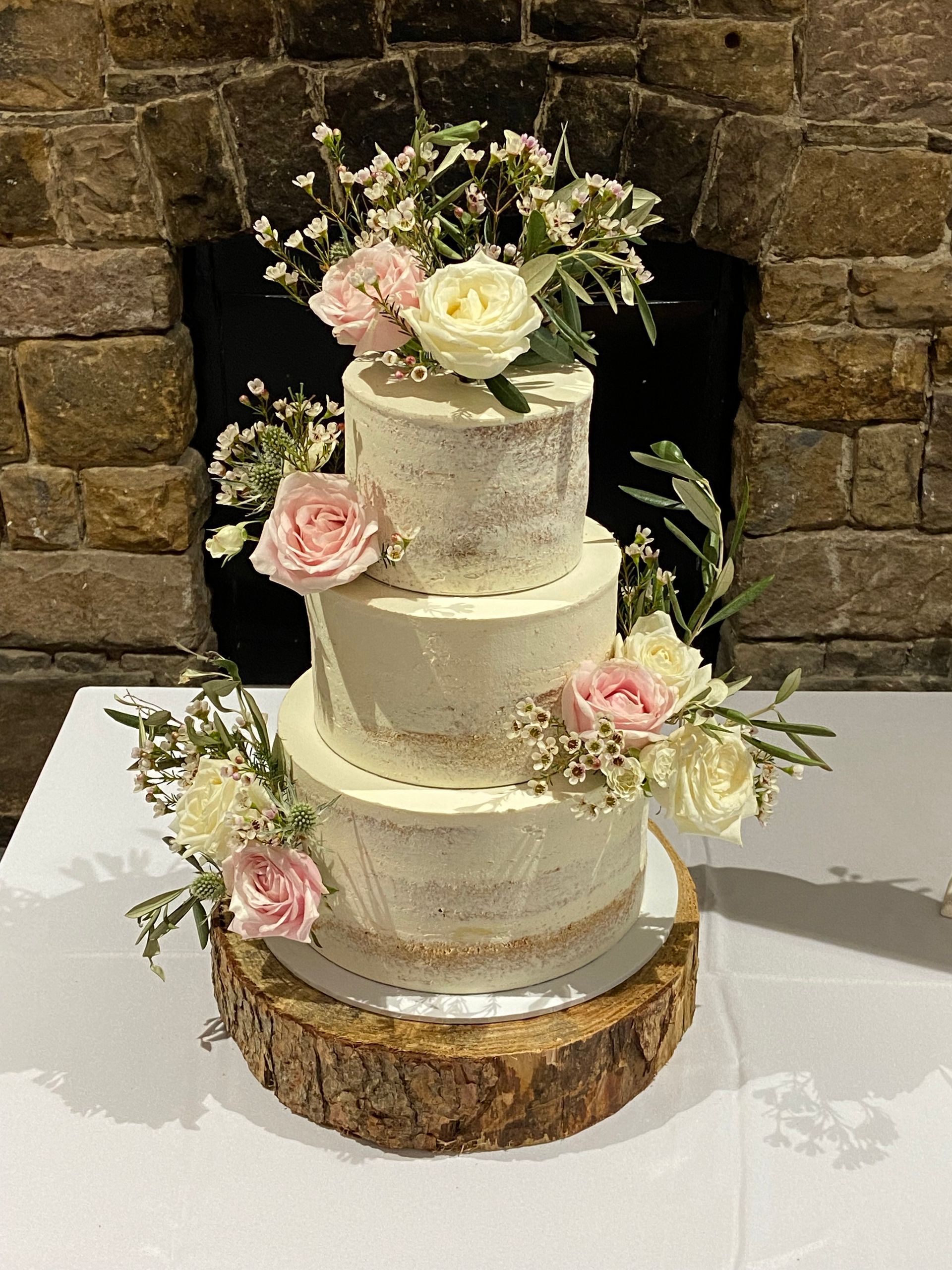 A wedding cake is sitting on top of a wooden stump on a table.