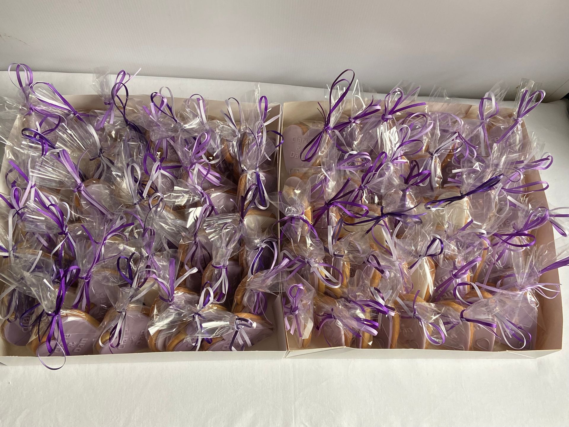 A box filled with purple ribbon wrapped cookies.