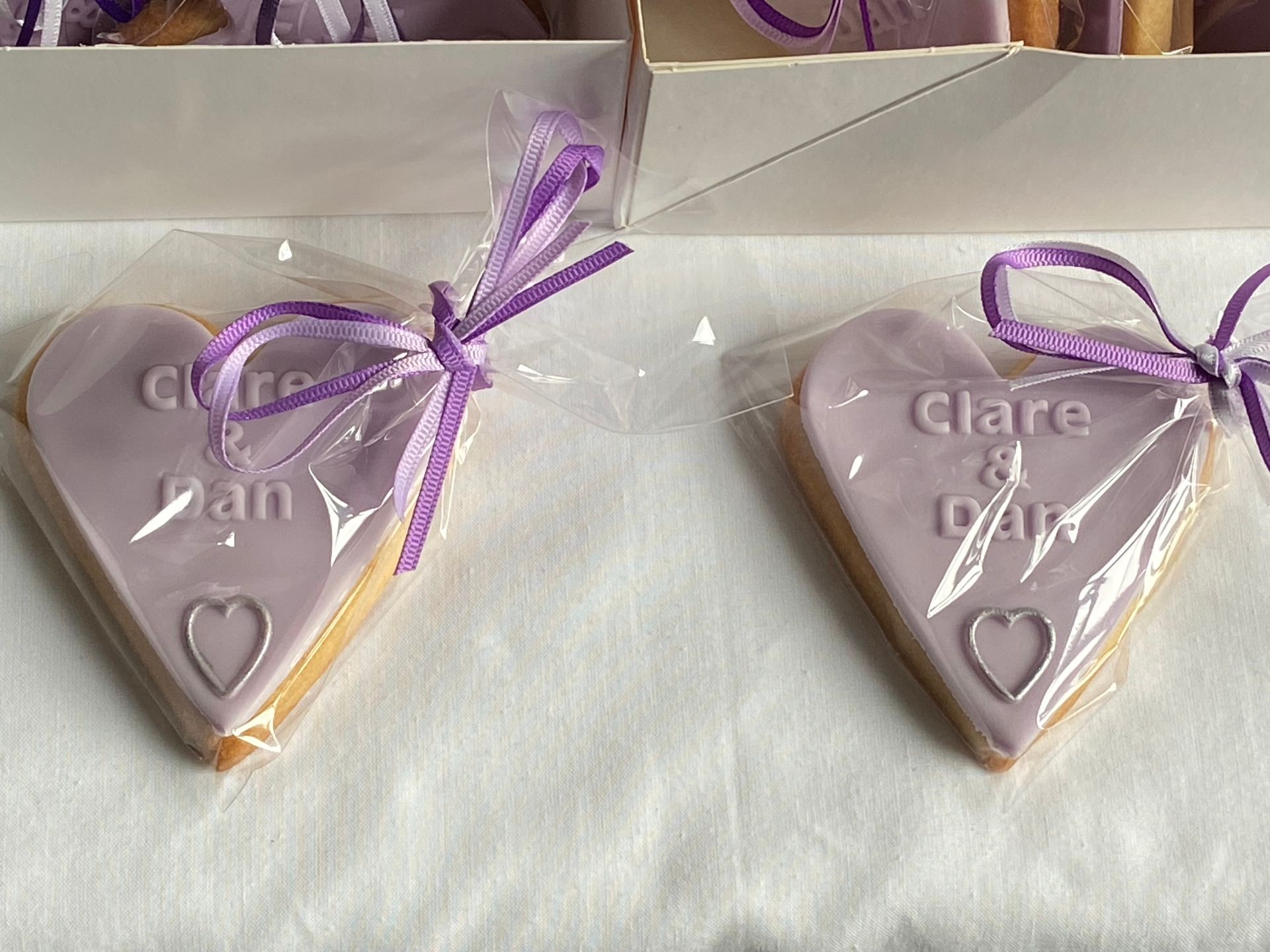 Two purple heart shaped cookies with the names clare and dan on them