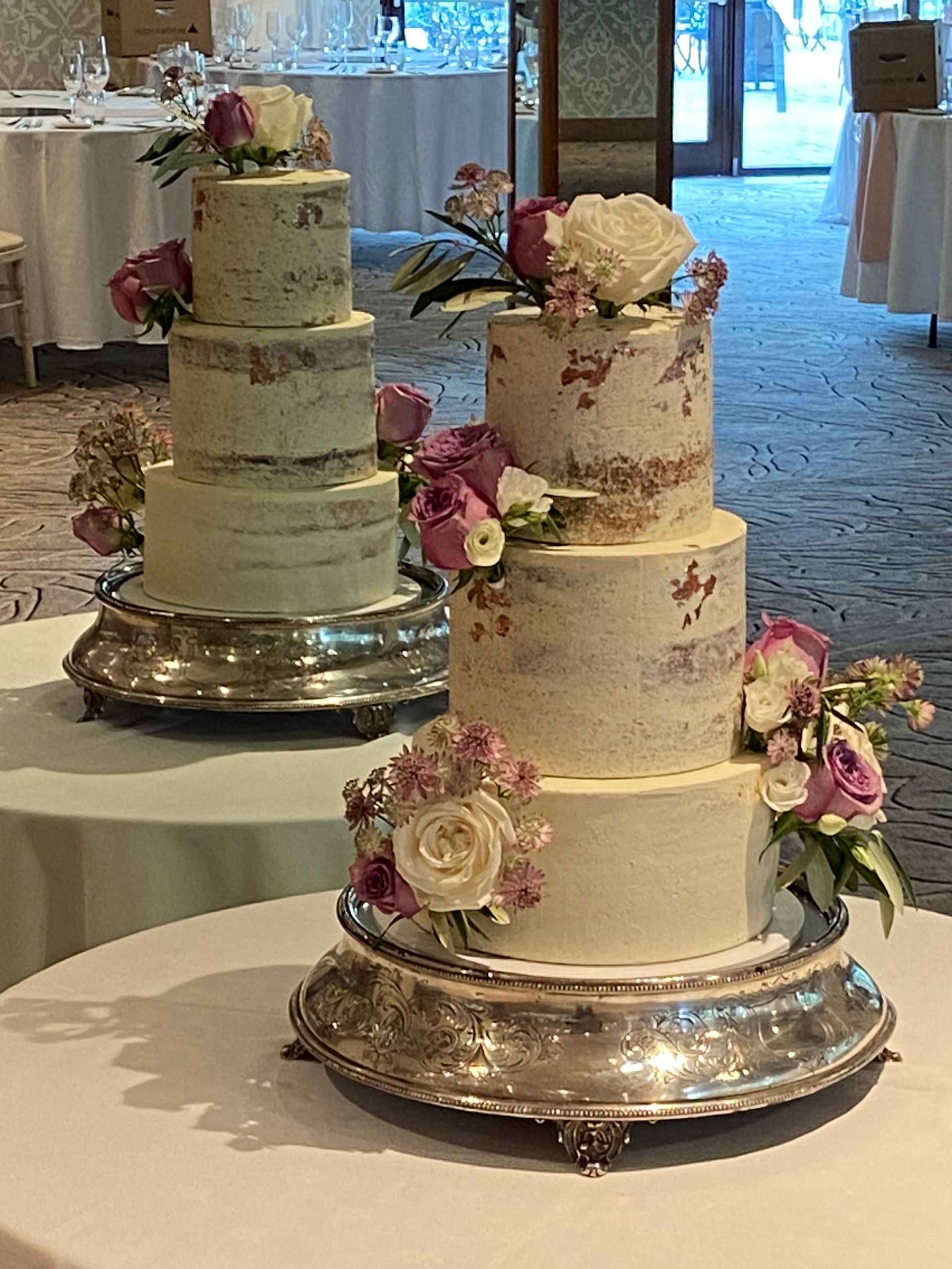 Two wedding cakes are sitting on top of a silver cake stand on a table.
