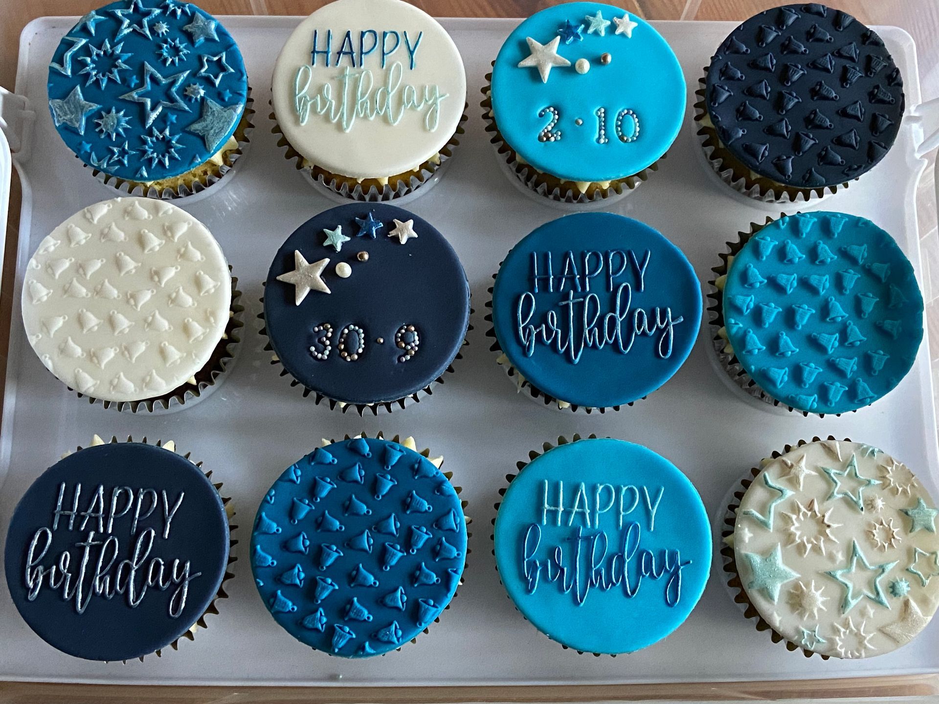 A tray of blue and white cupcakes with happy birthday written on them.