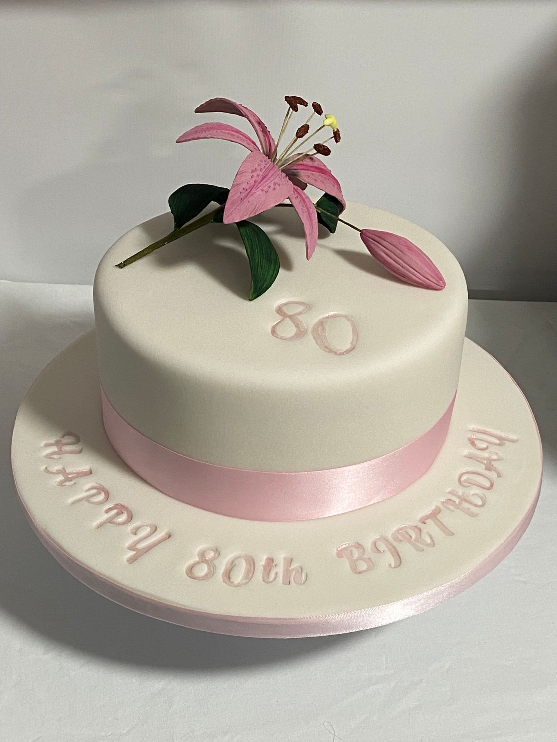 A white birthday cake with a pink flower on top