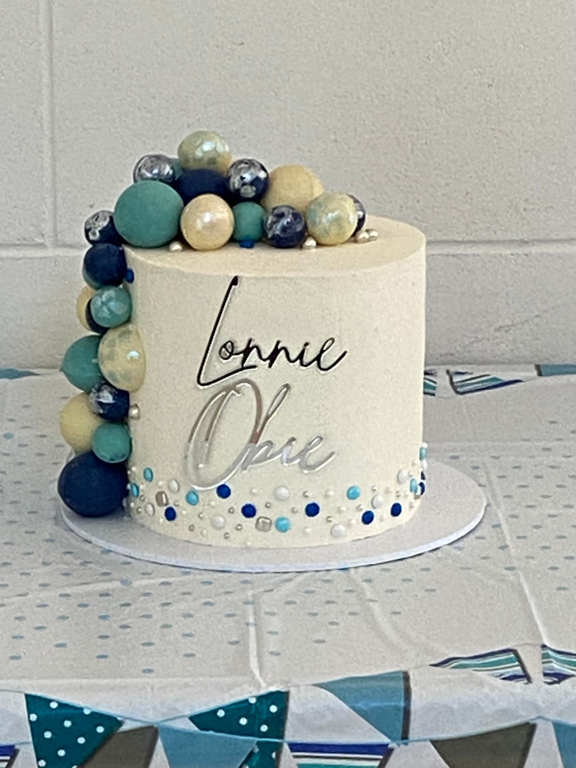 A white cake with blue and yellow balls on top is sitting on a table.