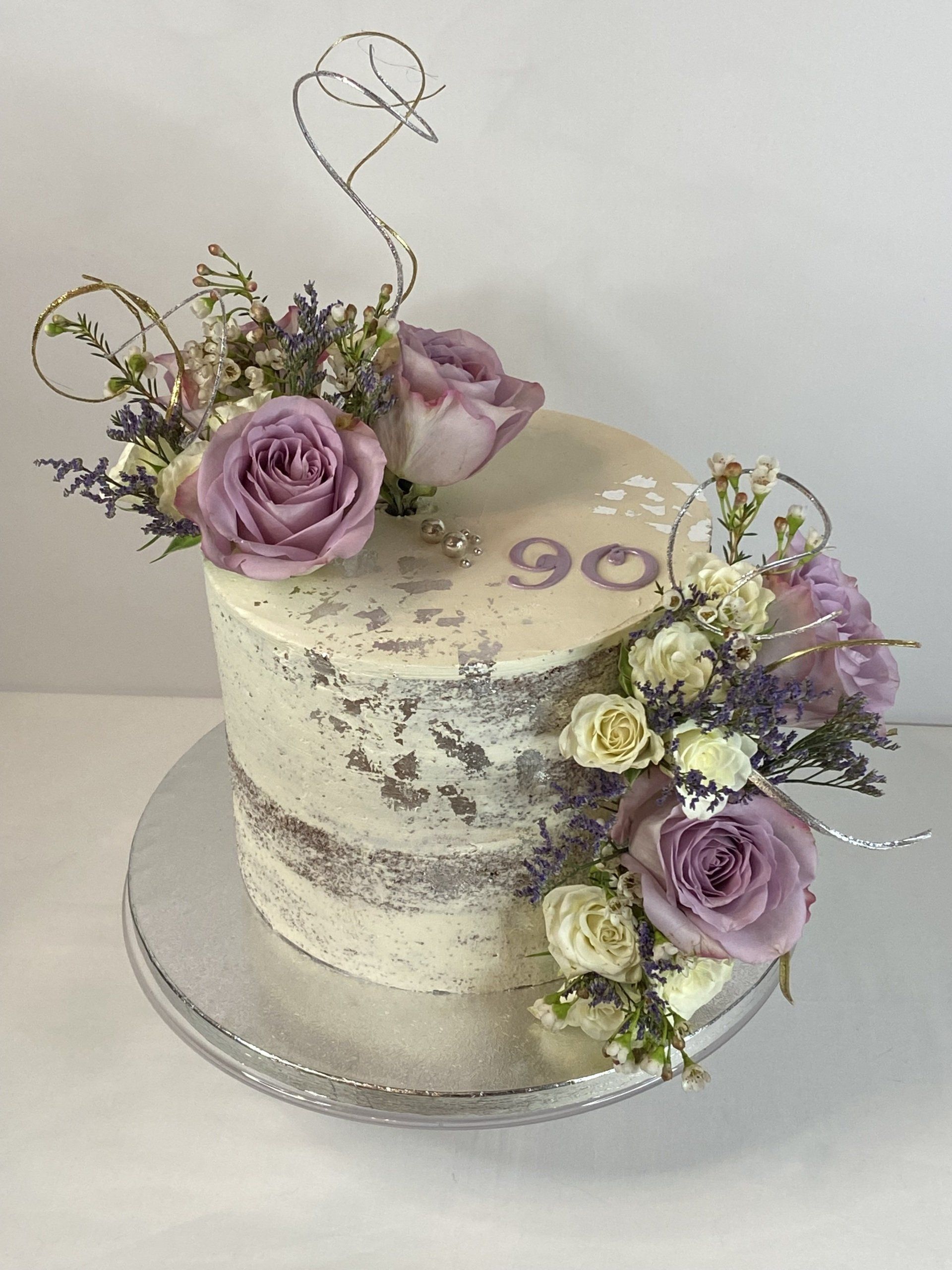 A cake with purple roses on top of it is on a silver plate.