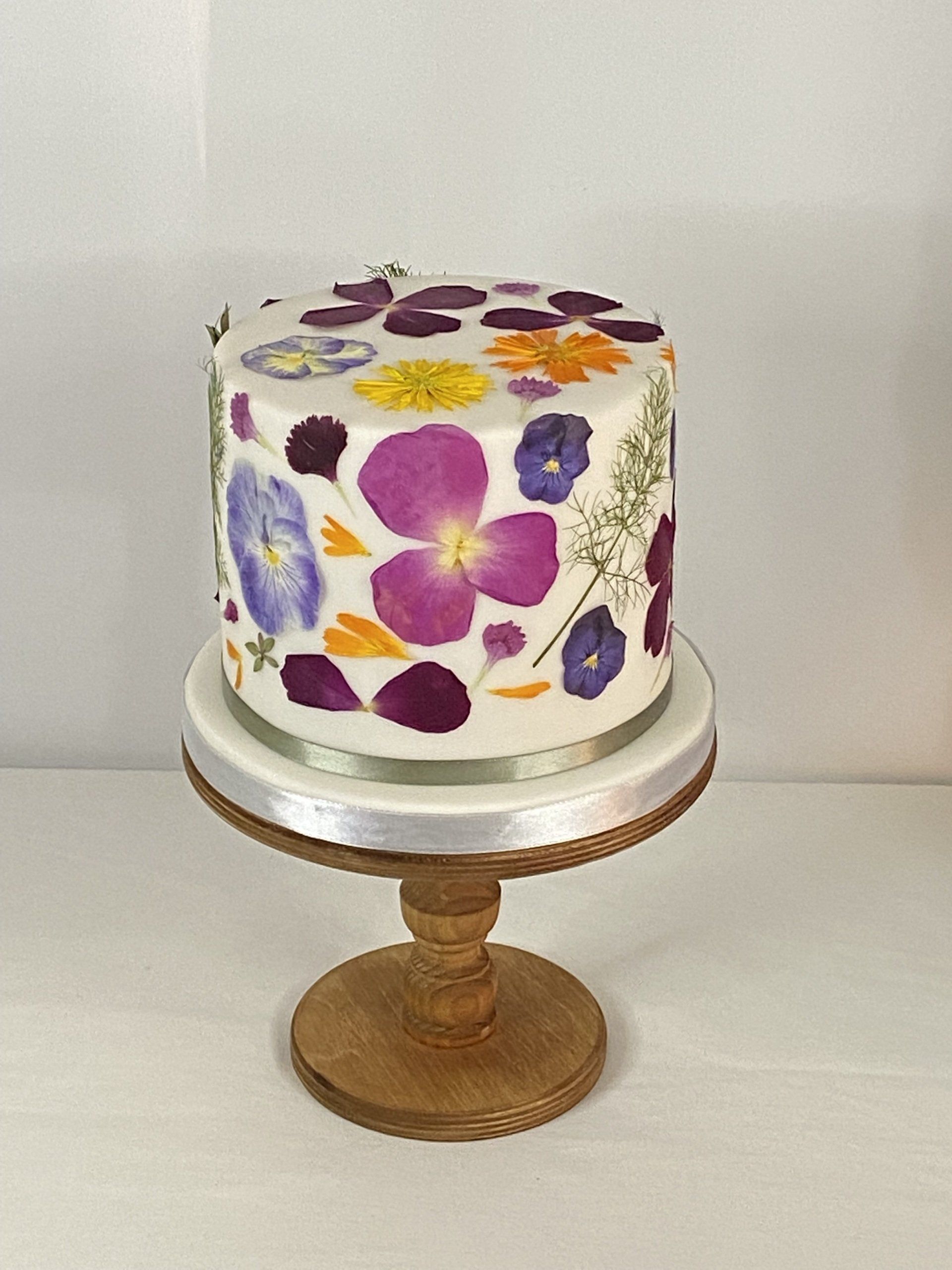 A cake with flowers on it is sitting on a wooden stand.