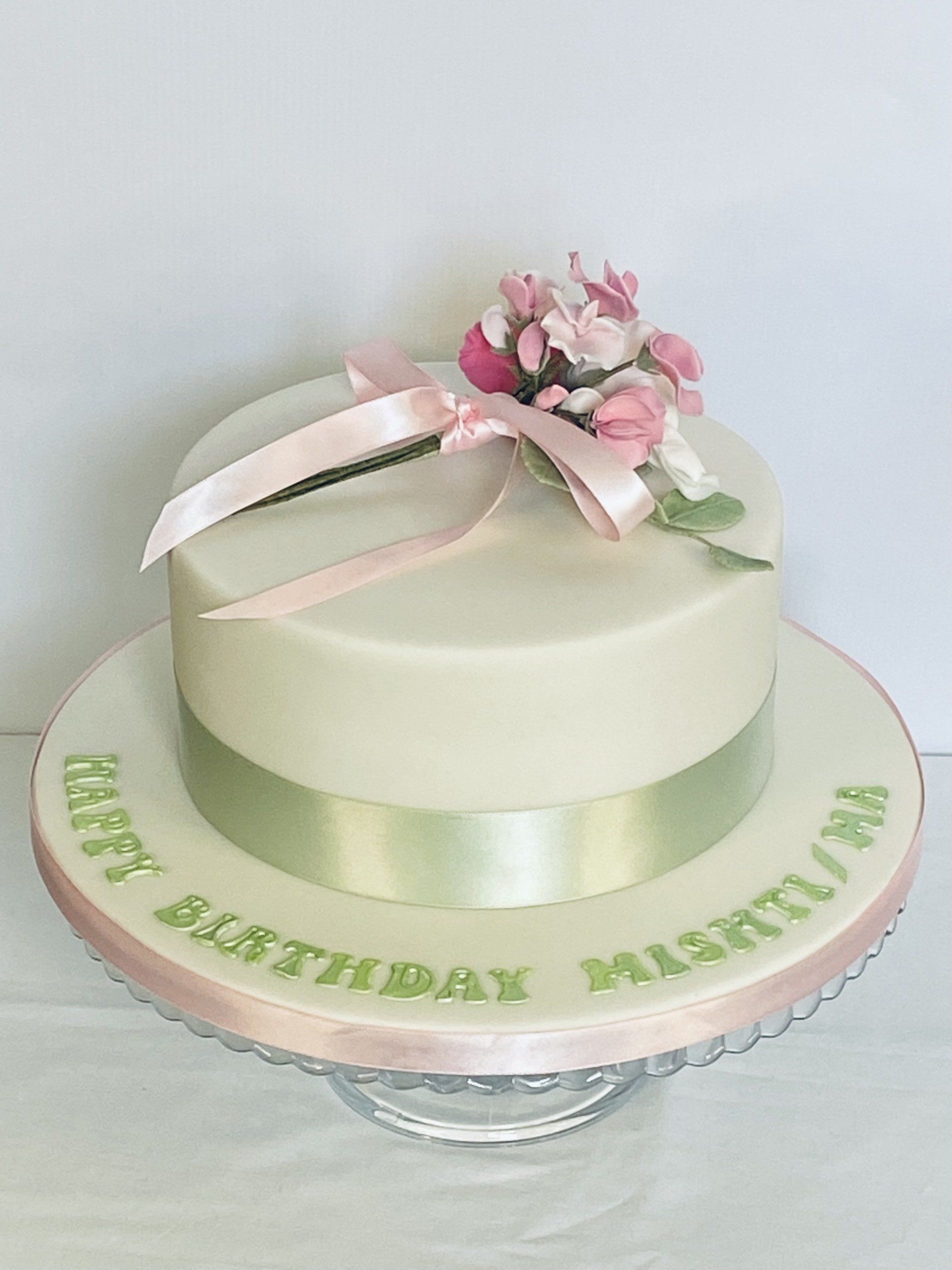 A birthday cake with a pink ribbon and flowers on it