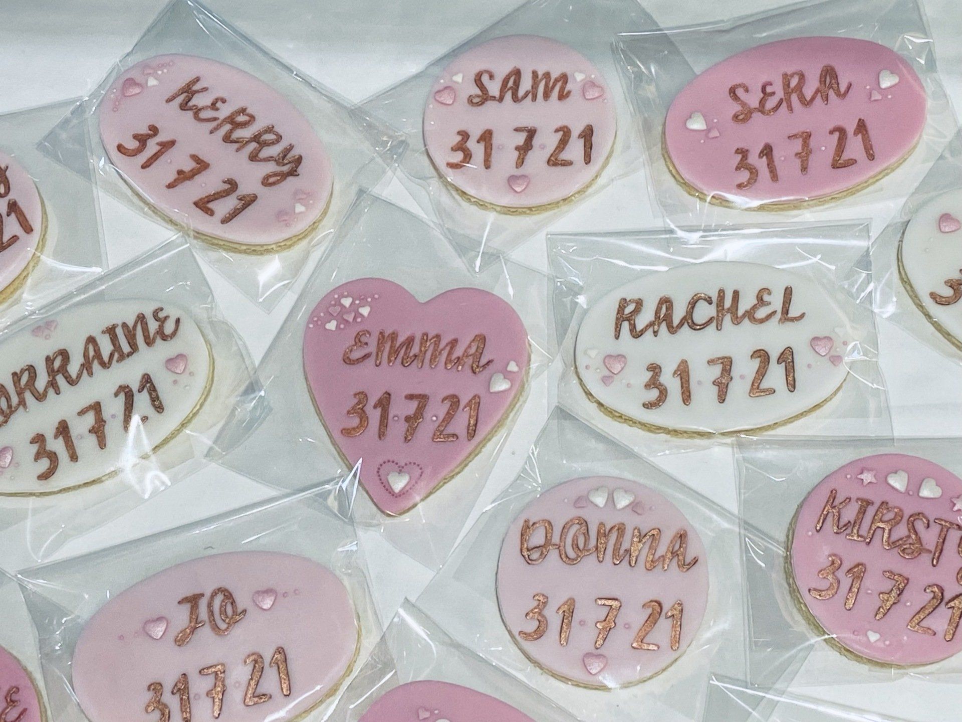 A bunch of pink and white cookies with names on them