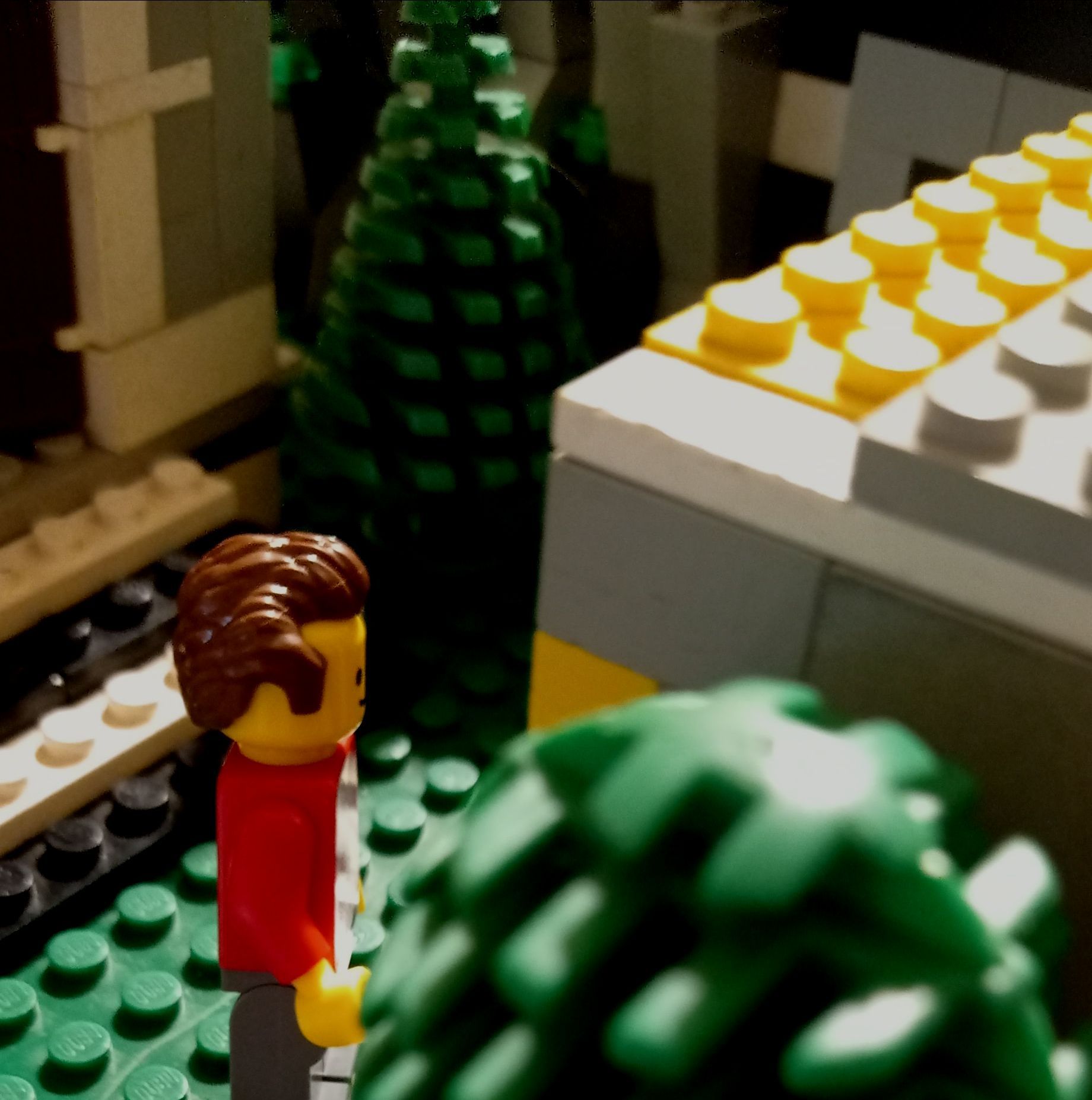 A lego figure in a red shirt is standing next to a tree