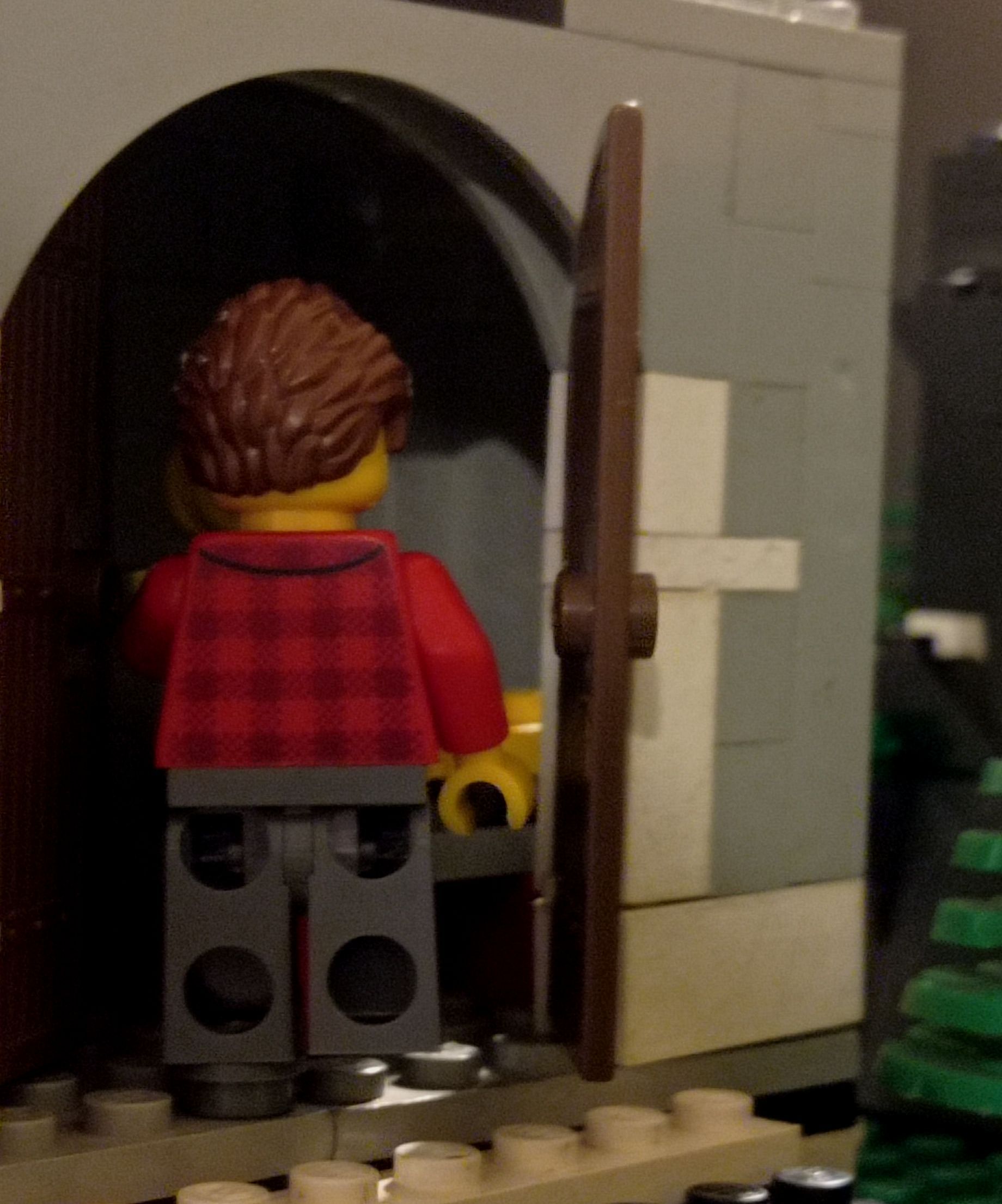 A lego figure in a red plaid shirt is standing in a doorway