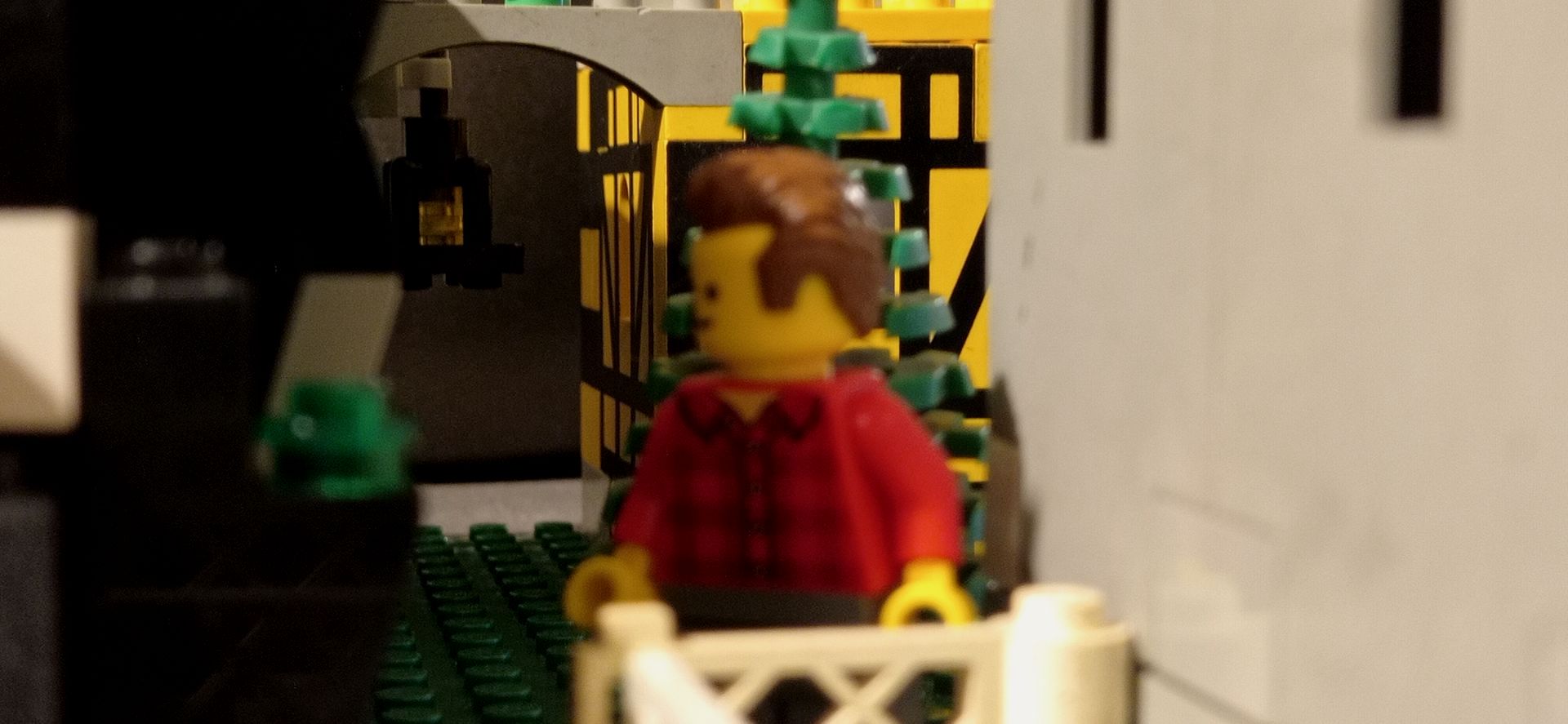 A lego man in a red shirt is standing next to a white fence.