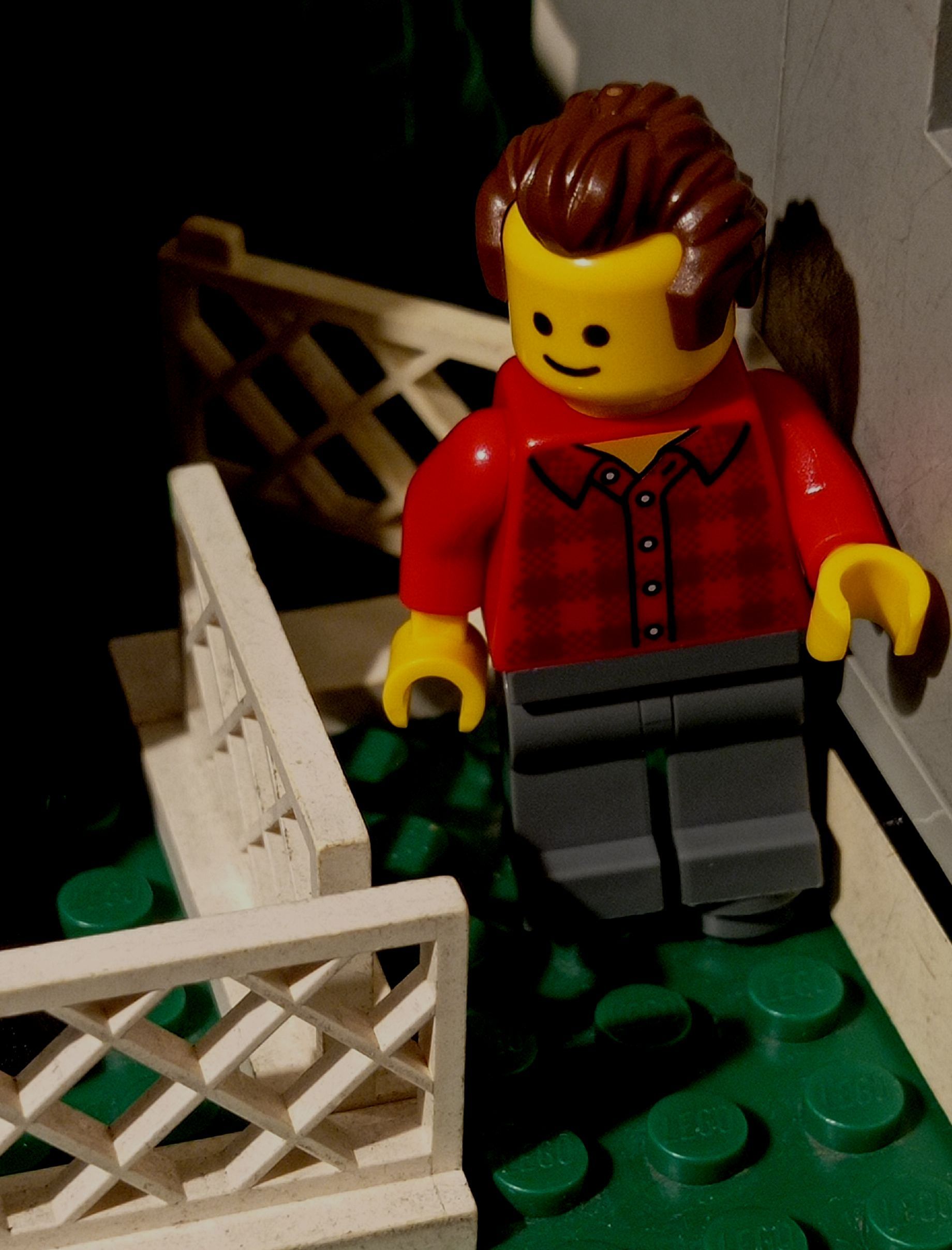 A lego man in a red shirt is standing next to a white fence