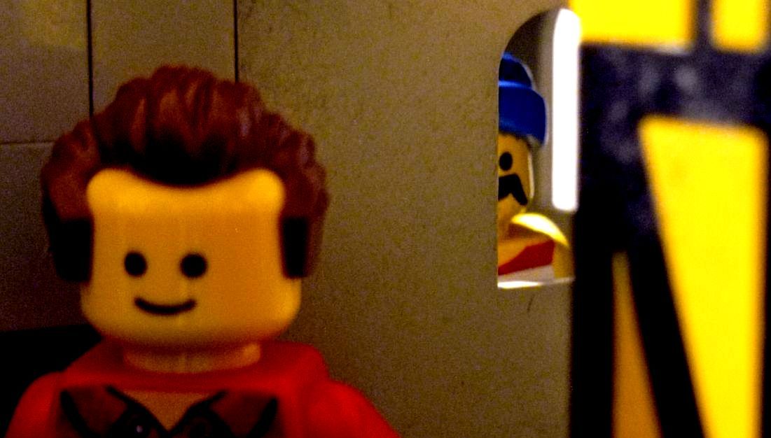 A close up of a lego man standing next to a window.