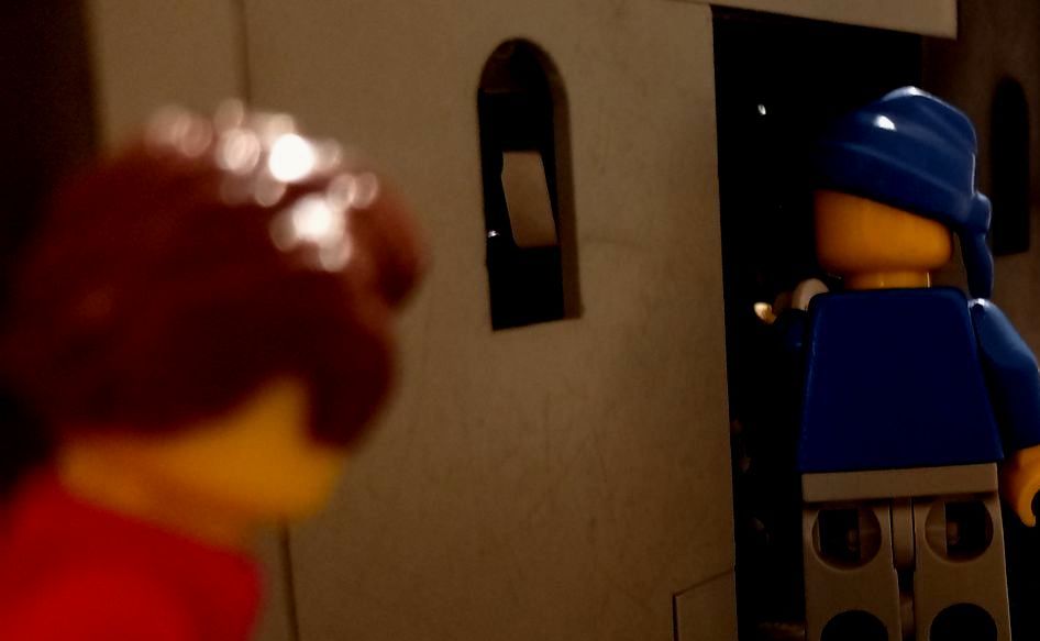 A lego man in a blue hat is standing in front of a building