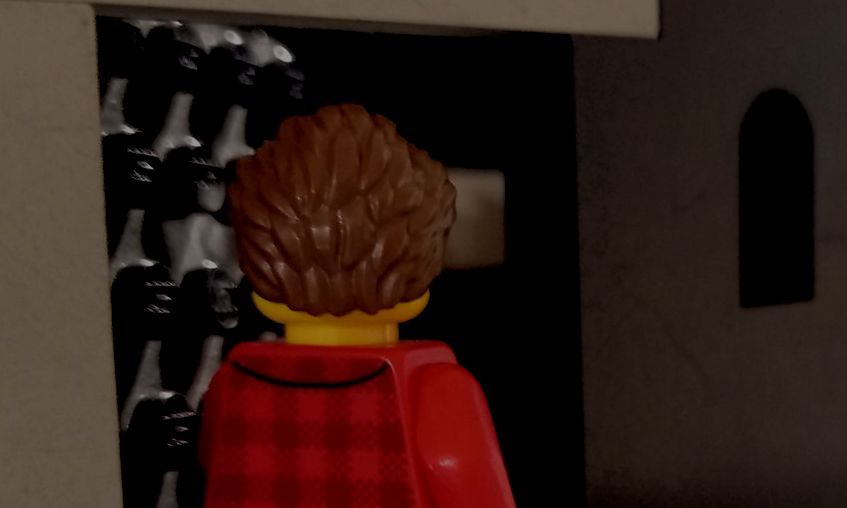 A lego man in a red cape is standing in a dark room.