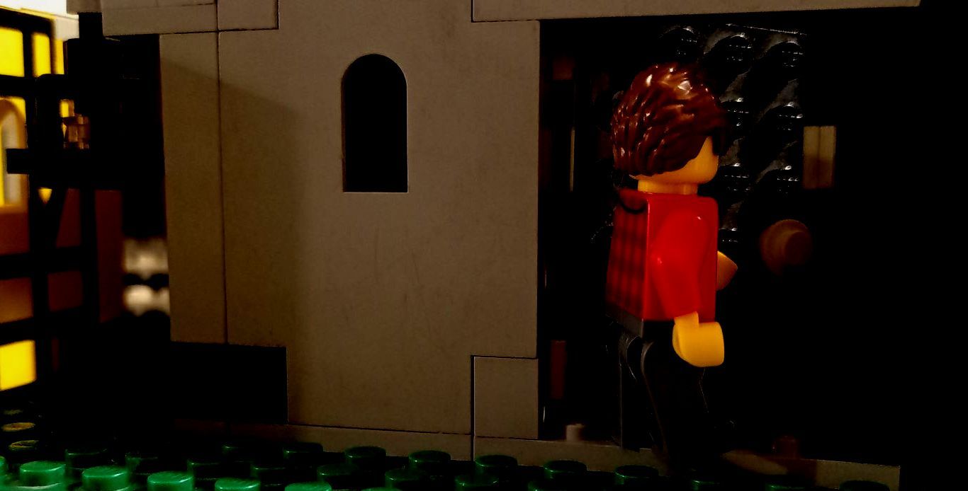 A lego figure is standing in front of a building in the dark.