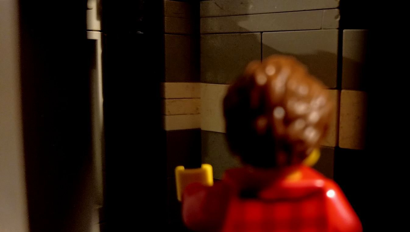 A lego man in a red jacket is standing in a dark room.