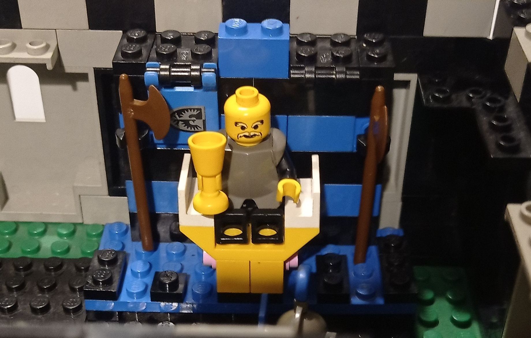 A lego figure is sitting on a throne holding a cup