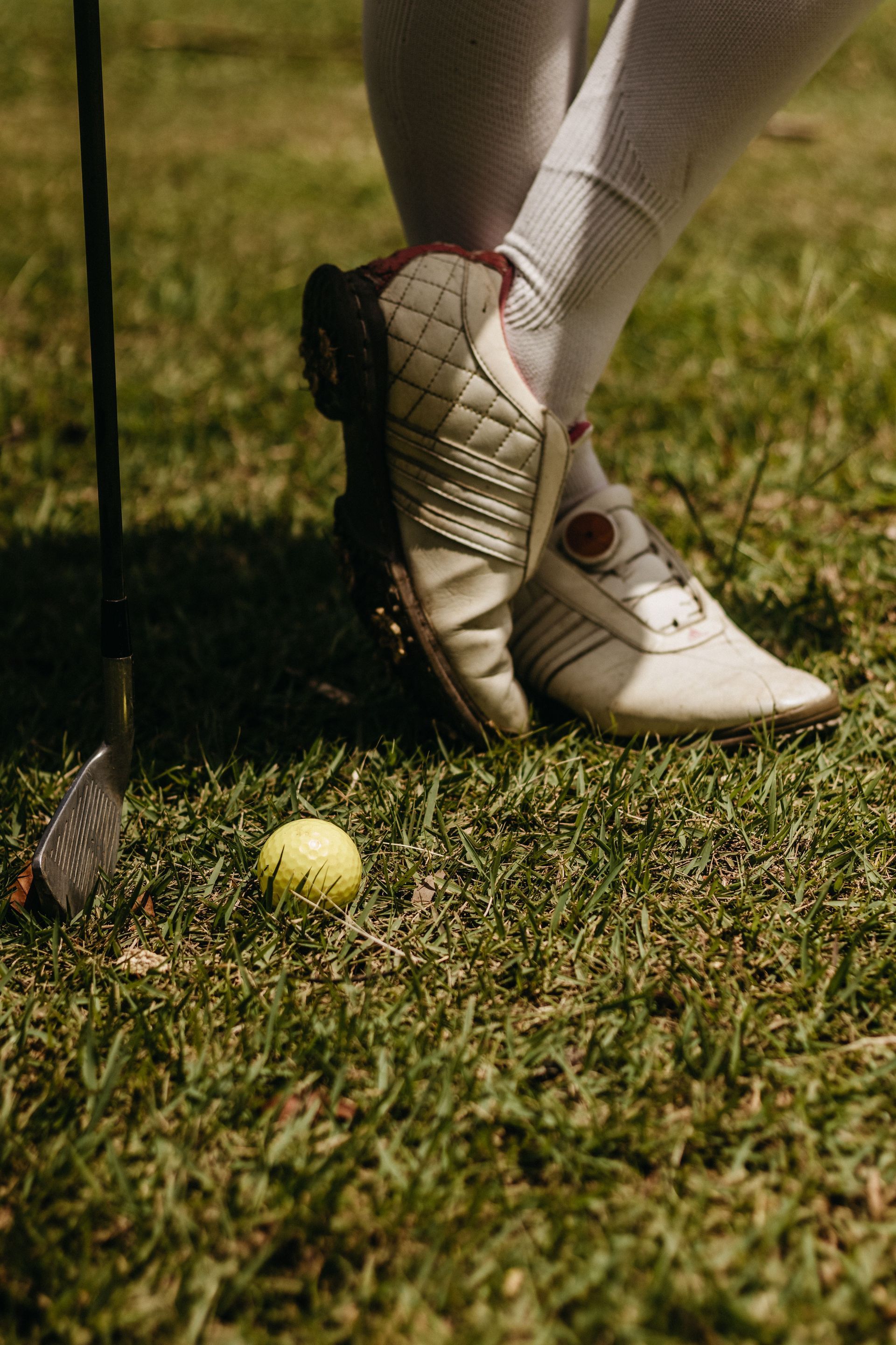 Close-up of a person in white socks and cleats standing near a yellow golf ball on grass