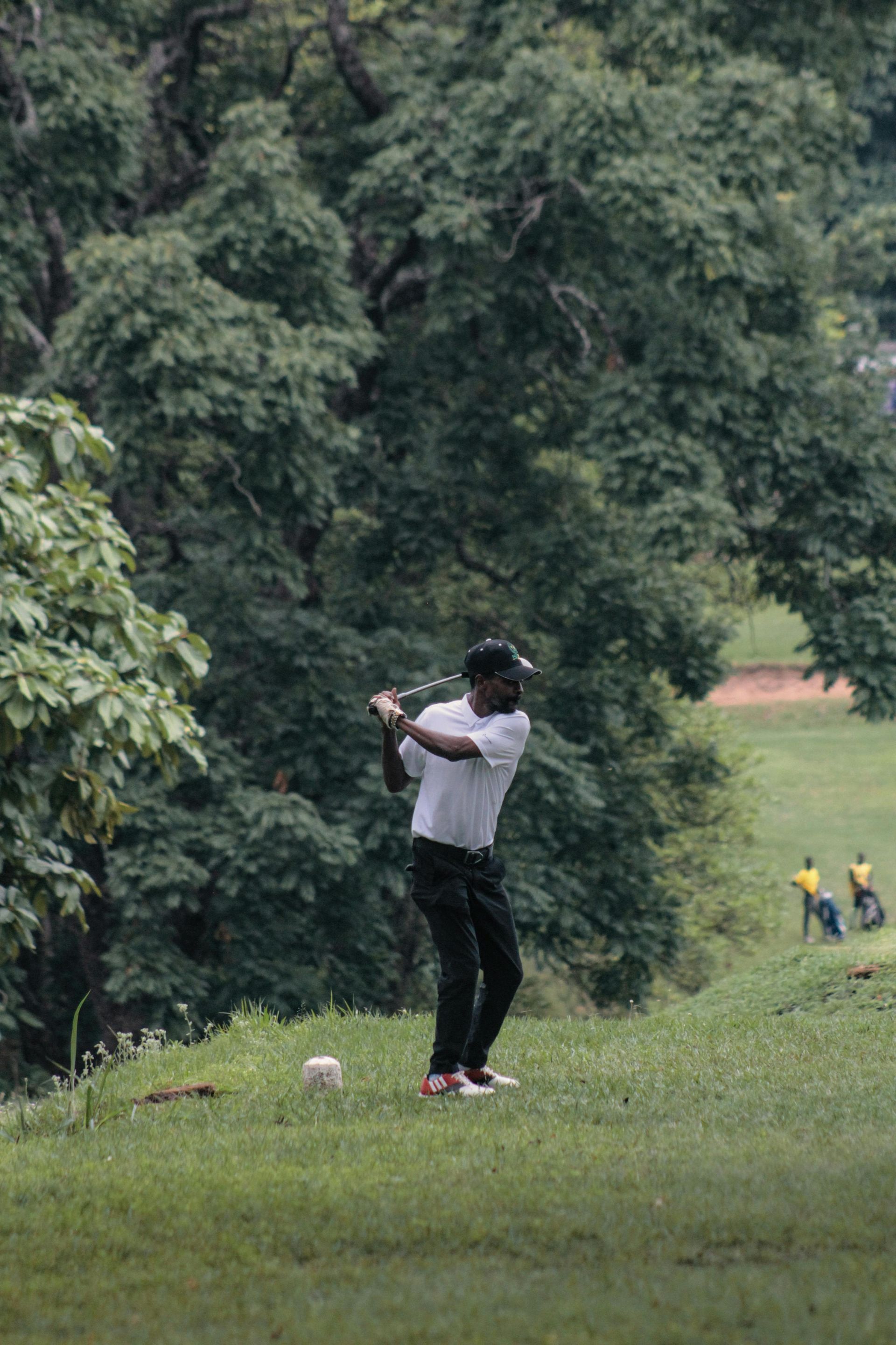 Golfer swinging a club on a grassy course beside dense trees