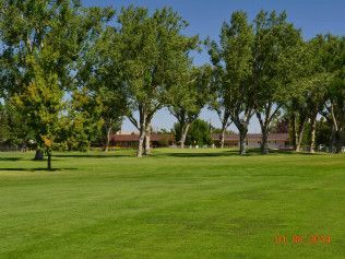 Green park lawn with trees and a red-roofed building in the background
