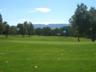 Sunny green golf course with trees, distant hills, and a blue sign on the fairway