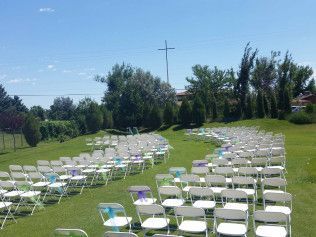 Rows of white folding chairs on a grassy lawn under a blue sky, set up for an outdoor event