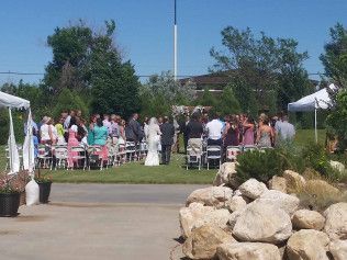 Outdoor wedding ceremony with guests seated on a lawn beside white tents and large rocks.