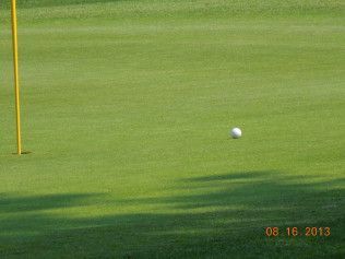 Golf ball on green near the yellow flagstick, with date stamp in the corner