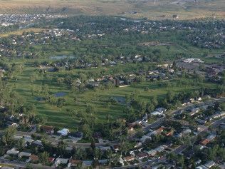 Aerial view of a green valley with fields, scattered houses, and distant hills under hazy light