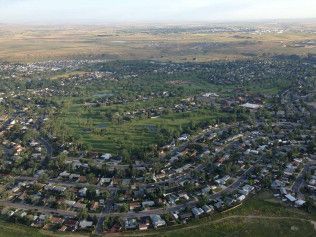 Aerial view of a suburban neighborhood with houses, streets, and green fields stretching into the distance.