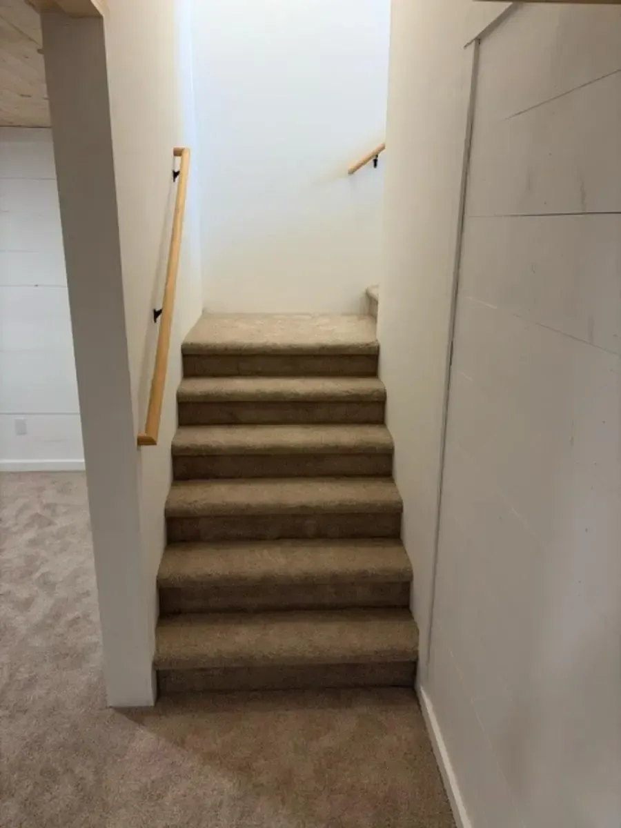 Carpeted indoor staircase with wooden handrail and white walls leading up to a landing