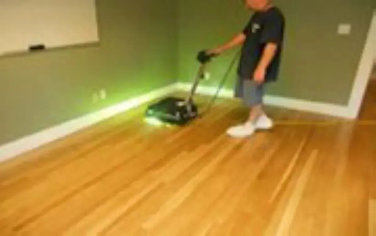 A boy is using a vacuum cleaner on a wooden floor