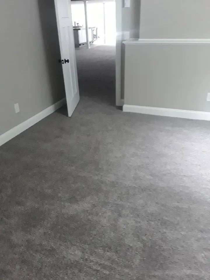 An empty room with a gray carpet and a door open.